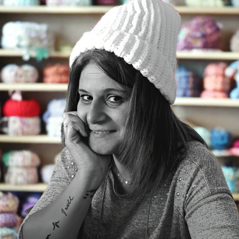 La creatrice de Fenicrochet tenant un sac en crochet, sourire et lunettes. Décor intérieur flou en arrière-plan.