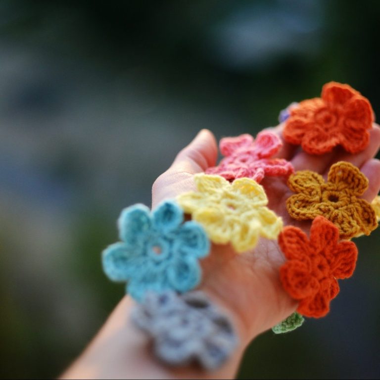 Un bras tenant des fleurs en crochet de différentes couleurs.