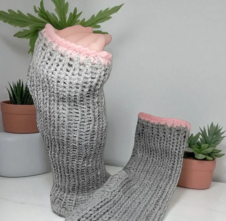 Mitaines en tricot grises avec une bordure rose, posées sur une surface claire.