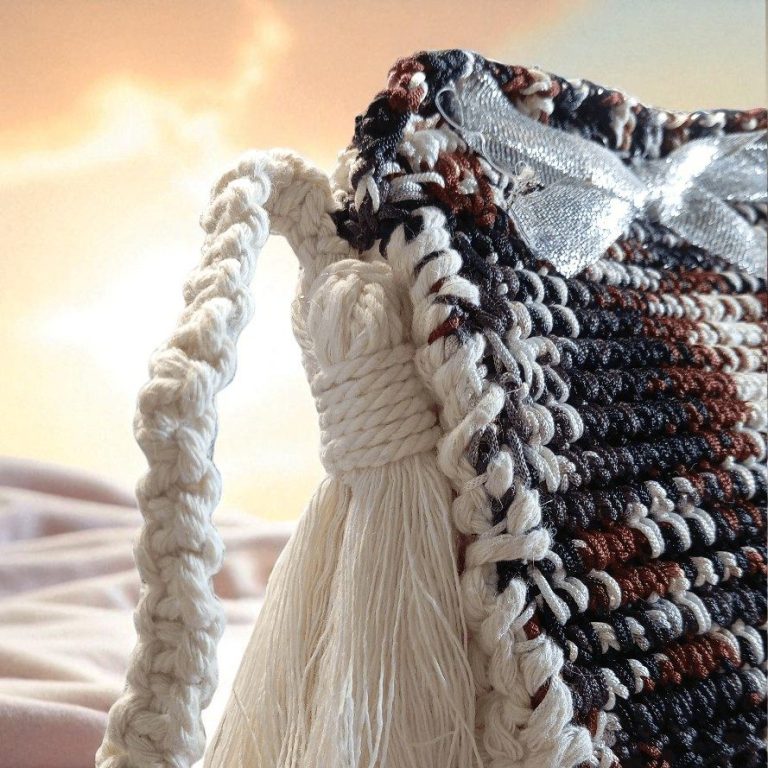 Sac en macramé avec un fini en franges et un ruban, éclairé par un coucher de soleil. FeniCrochet