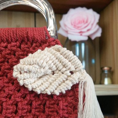 Sac à main rouge avec un détail de feuille en crochet et une rose en arrière-plan.