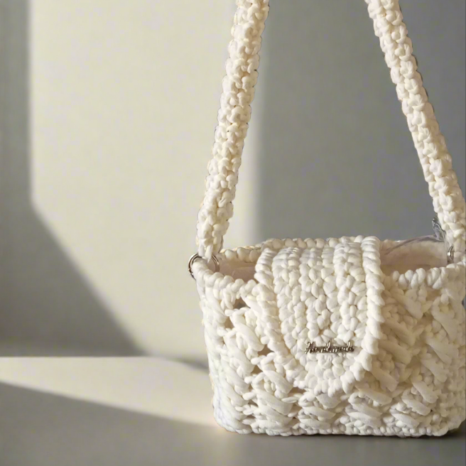 Sac à main au crochet blanc sur une surface claire, avec une ombre douce.