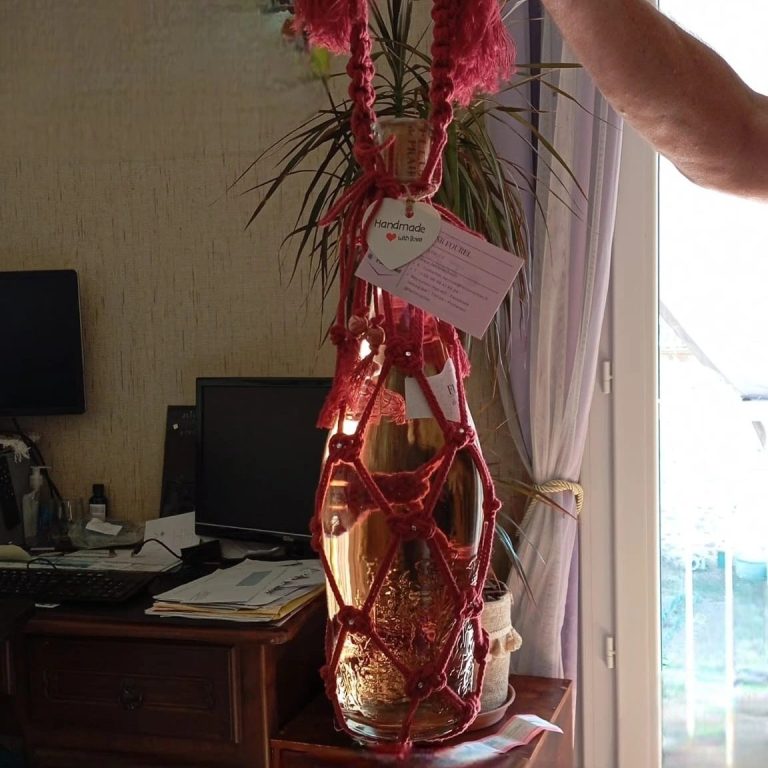 Bouteille de vin FeniCrochet entourée d'un filet en corde, suspendue par une main.