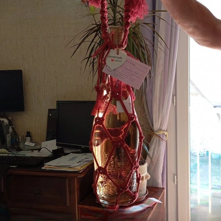 Porte bouteuille de vin Fencrochet Bouteille de vin nouée avec une corde rose, posée sur une table près d'un ordinateur.